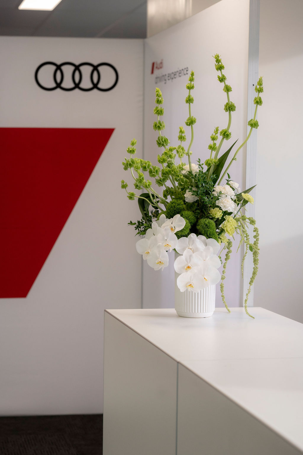 Large vase of green and white flowers on console in front of Audi branding, made by Morrie & Maisie Event Flowers in Melbourne